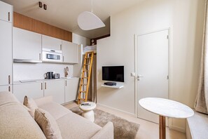 A compact living space with a kitchenette, a sofa, a small table, and a TV mounted on the wall. - Montmartre-Mobility lease-Studio-2 persons-Renovated (Paris)