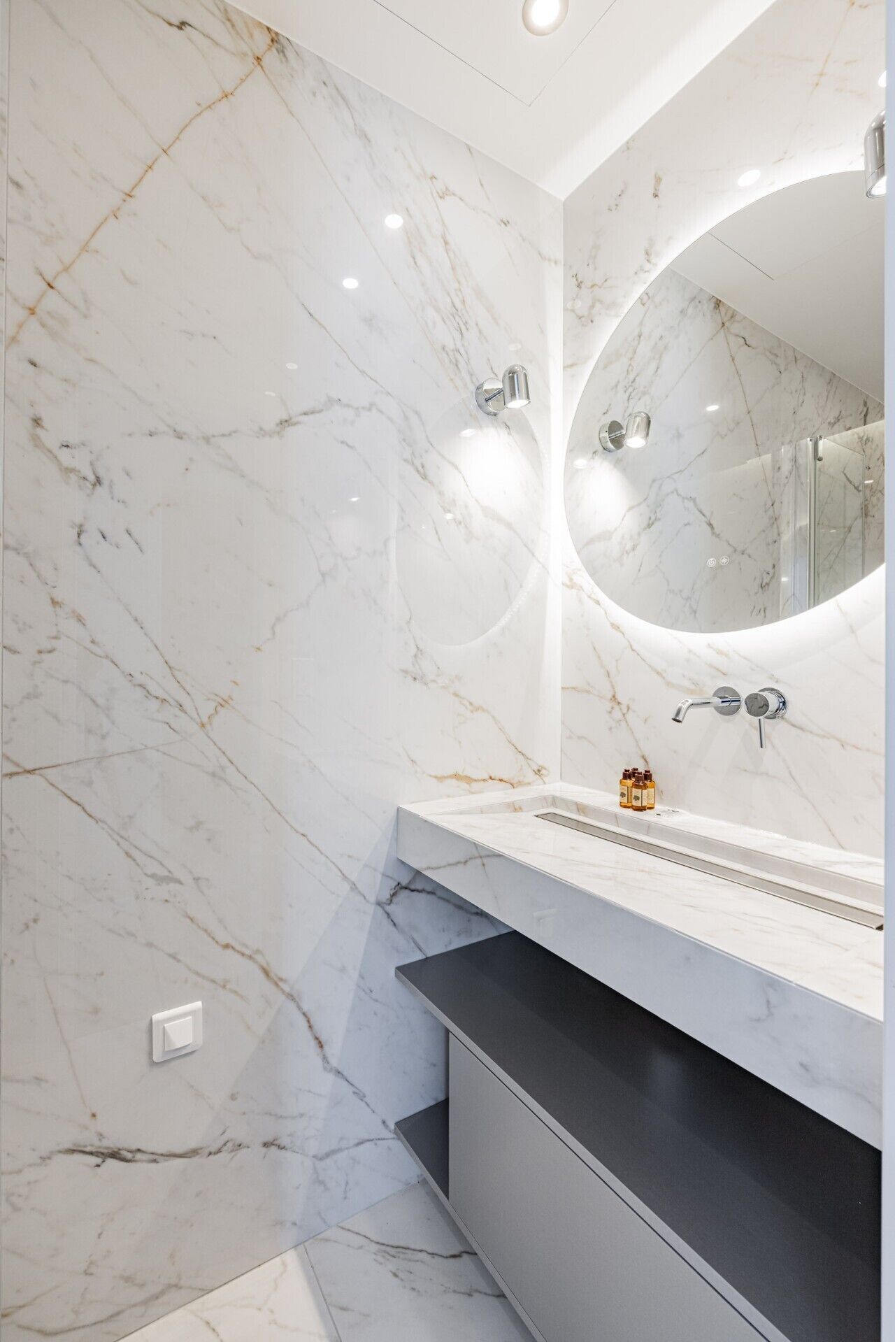 A modern bathroom with marble walls, a large mirror, a built-in sink, and a shower enclosure.