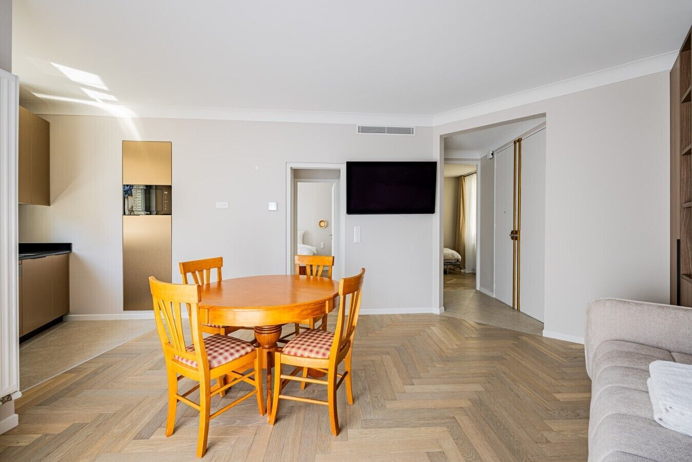 A dining area with a round table and chairs, a kitchen with a microwave, and a TV mounted on the wall.
