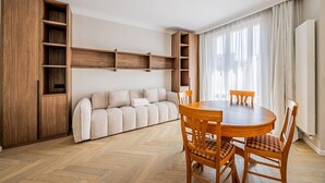Un soggiorno moderno con divano, tavolo da pranzo in legno, sedie, scaffalature integrate in legno e un termosifone.