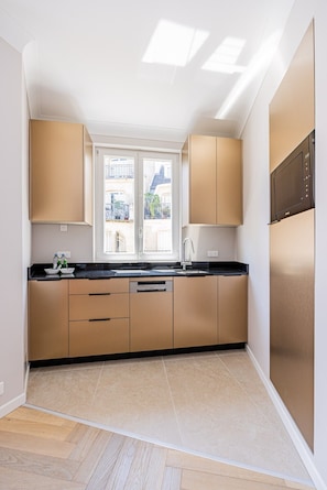 A modern kitchen with a large window, wooden cabinets, and a built-in oven. - Premium-New mobility lease-Paris16th-2bedroom (Paris)