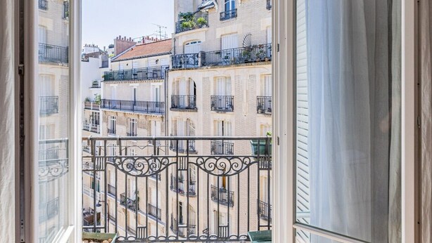 Un balcone aperto con vista sugli edifici circostanti, ringhiera in metallo e pavimento in legno.