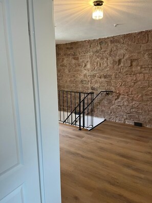 Una habitación con pared de piedra, suelo de madera y escalera de metal negro.