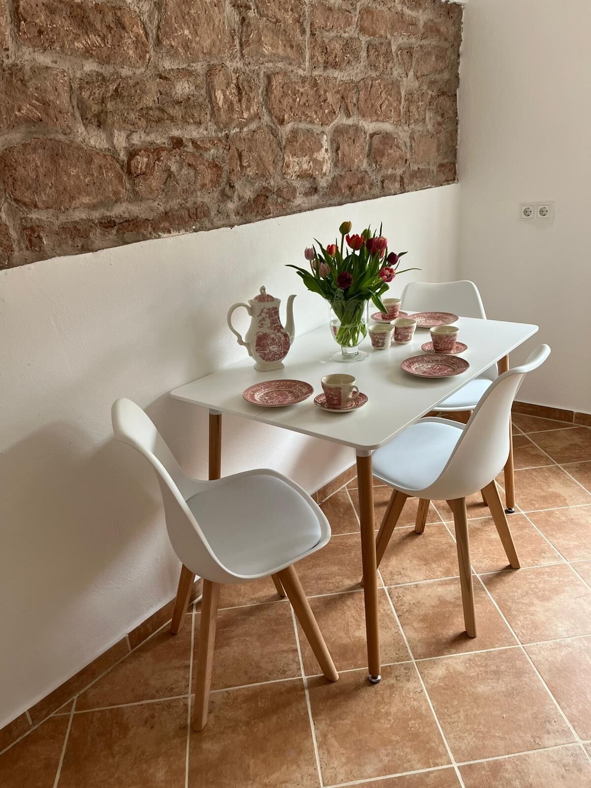 Una mesa de comedor con sillas blancas, un jarrón de flores y juego de té a juego.