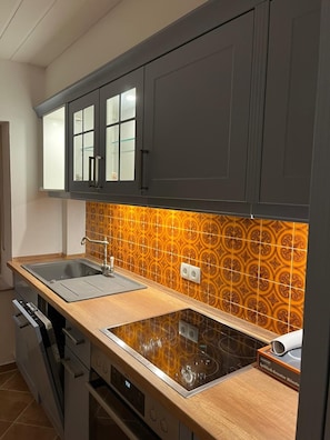 A kitchen with dark cabinets, a double sink, a built-in oven, and a patterned backsplash.