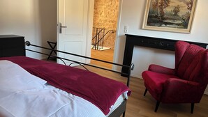 A bedroom with a bed, a red chair, a fireplace, and a painting on the wall. - Our small chalet in the heart of the Palatinate Forest. Relaxation, hiking, romance. (Lindenberg)