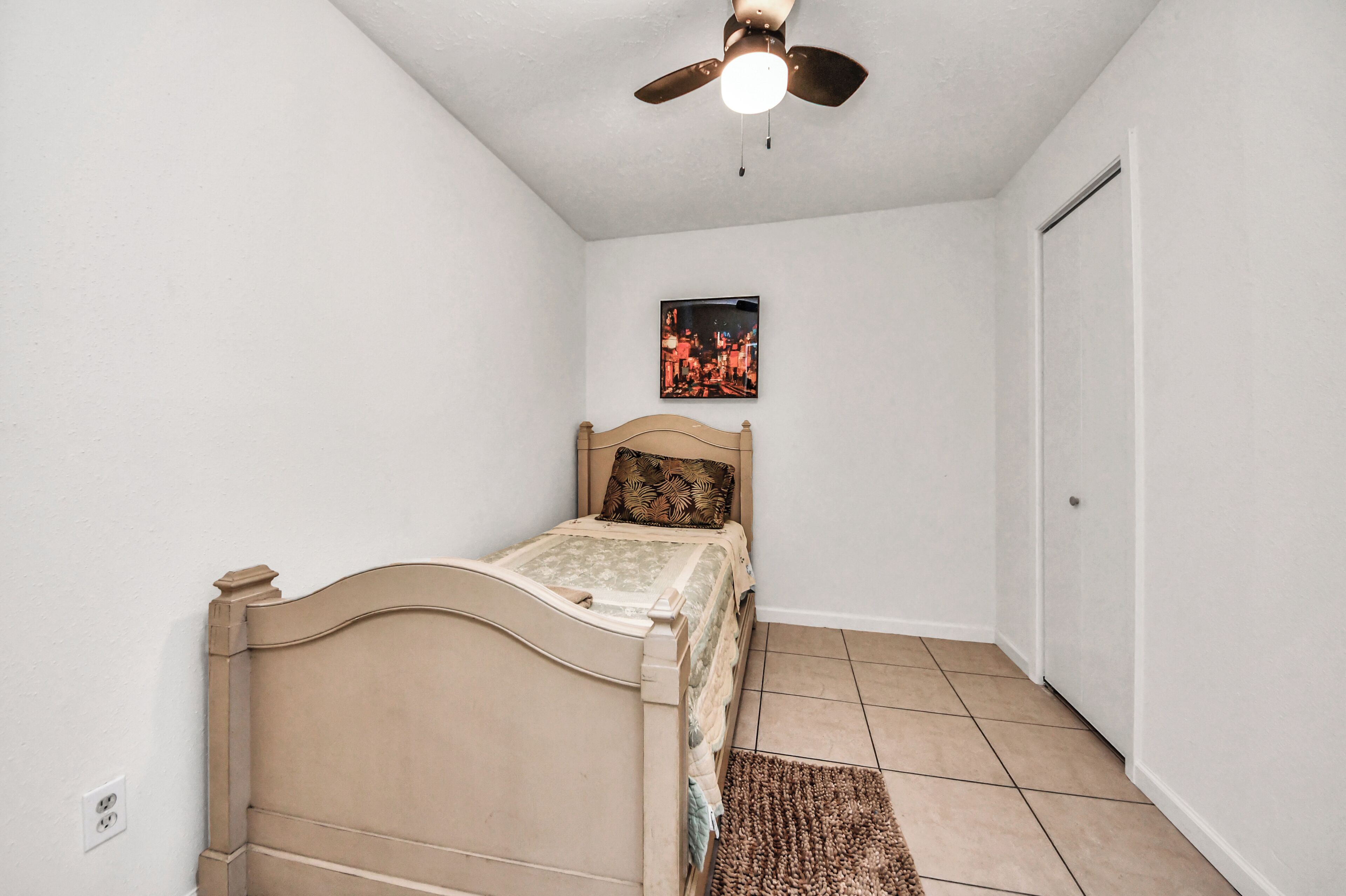 A bedroom with a bed, a ceiling fan, a door, and a wall-mounted picture.