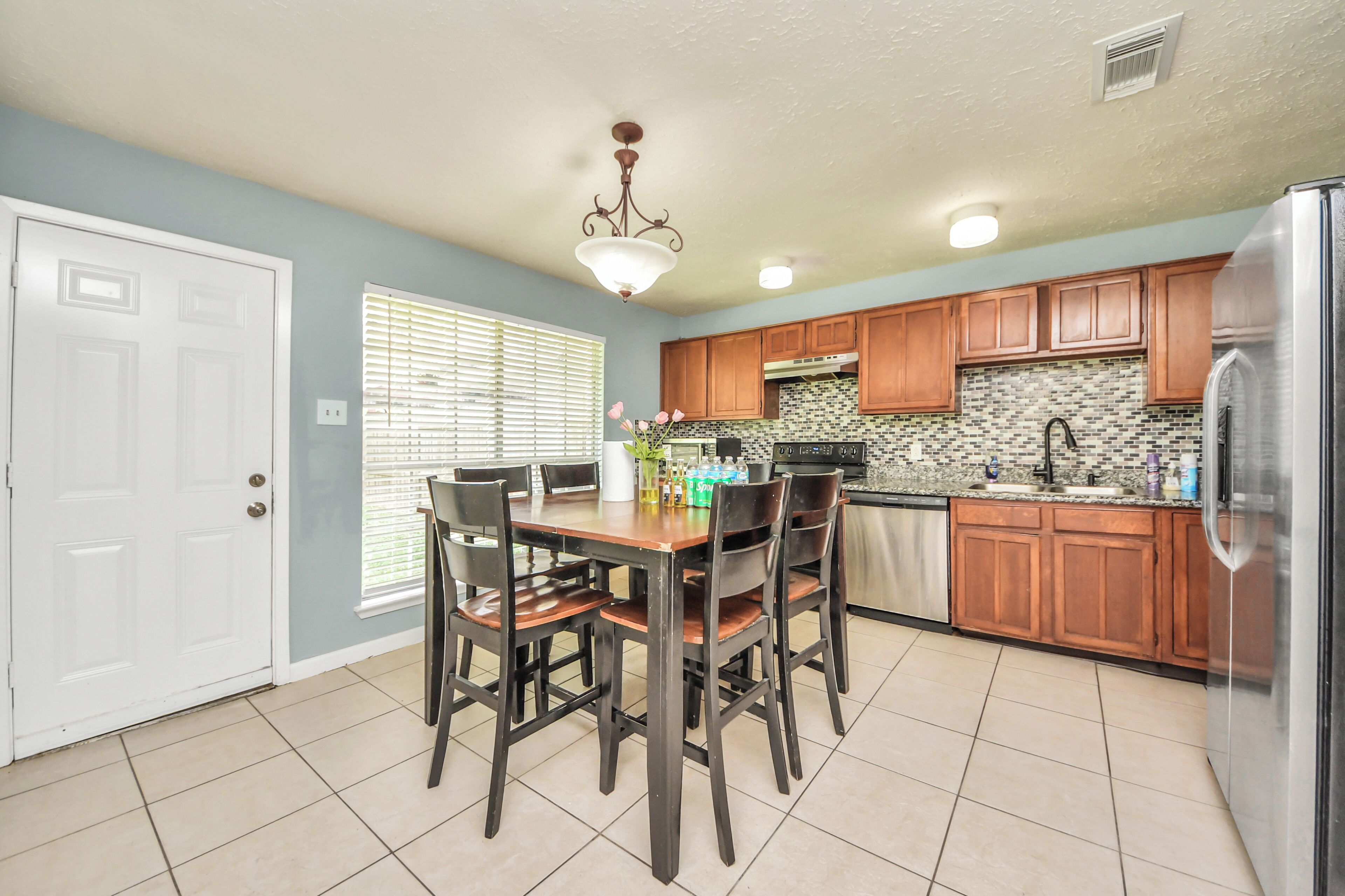 A kitchen with wooden cabinets, a stainless steel refrigerator, and a dining table with chairs.