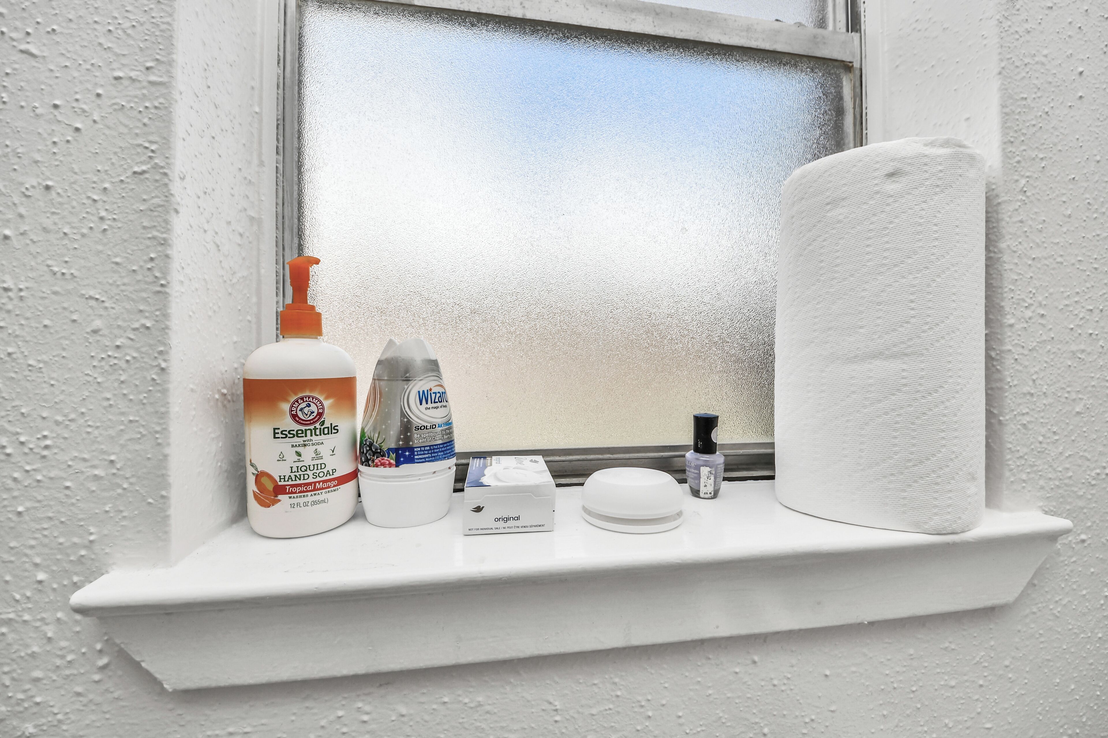 Uno scaffale in bagno con una bottiglia di sapone per le mani, una bottiglia di Windex, una confezione di carta igienica e una piccola bottiglia di lozione.