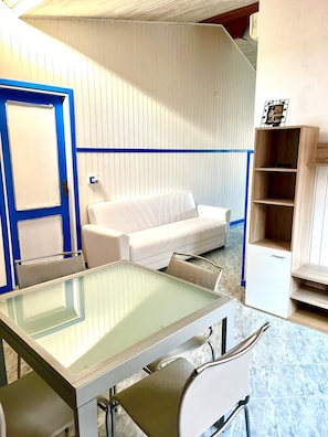 A room with a white sofa, a glass-top table, and a blue-framed door. - Calasetta Sottotorre (Calasetta)