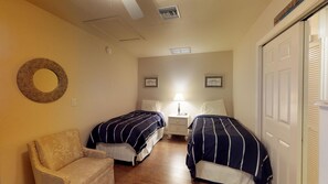 Una camera d'albergo con due letti, una sedia, un comodino con lampada e uno specchio fissato alla parete.