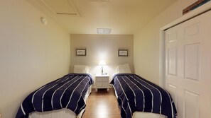 A narrow hallway with two single beds, a nightstand with a lamp, and a door on the right. - Driftwood Landing 18- Isles of Capri Vacation Resort. (Naples)
