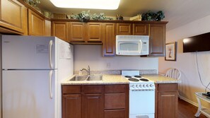 A kitchen with wooden cabinets, a white refrigerator, a microwave, a sink, and a stove. - Driftwood Landing 18- Isles of Capri Vacation Resort. (Naples)
