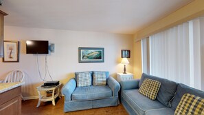 A living room with a blue sofa, a white chair, a small table with a lamp, and a television on the wall. - Driftwood Landing 18- Isles of Capri Vacation Resort. (Naples)