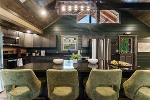 A modern kitchen with a central island, bar stools, stainless steel appliances, and a view through a window. - Pool, Hot tub, Game Room, Gazebo, Sleeps 36 (Sevierville)