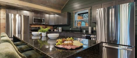A modern kitchen with stainless steel appliances, a marble countertop, and a built-in island with a food display.