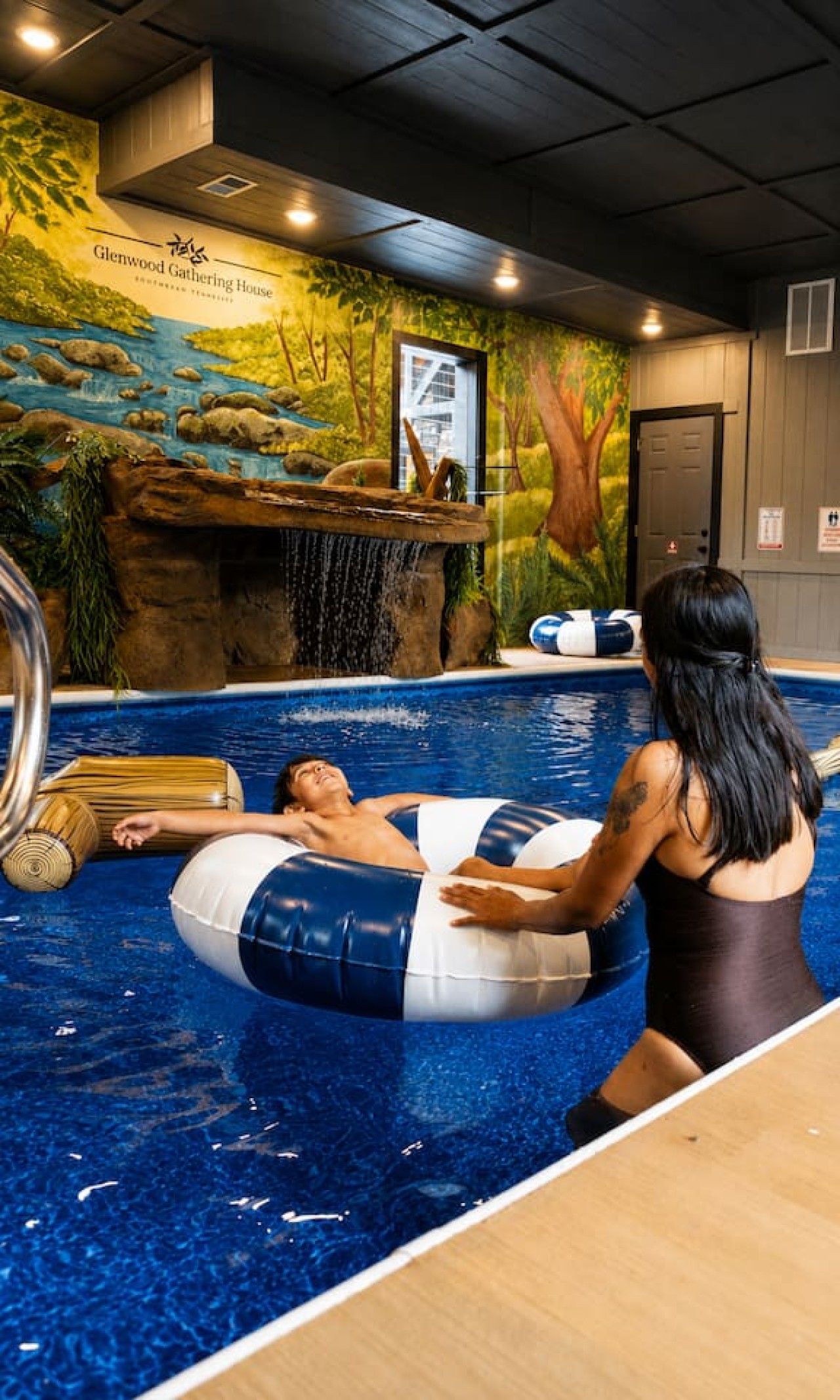 A pool area with a mural of a forest scene, a wooden bench, and a door.