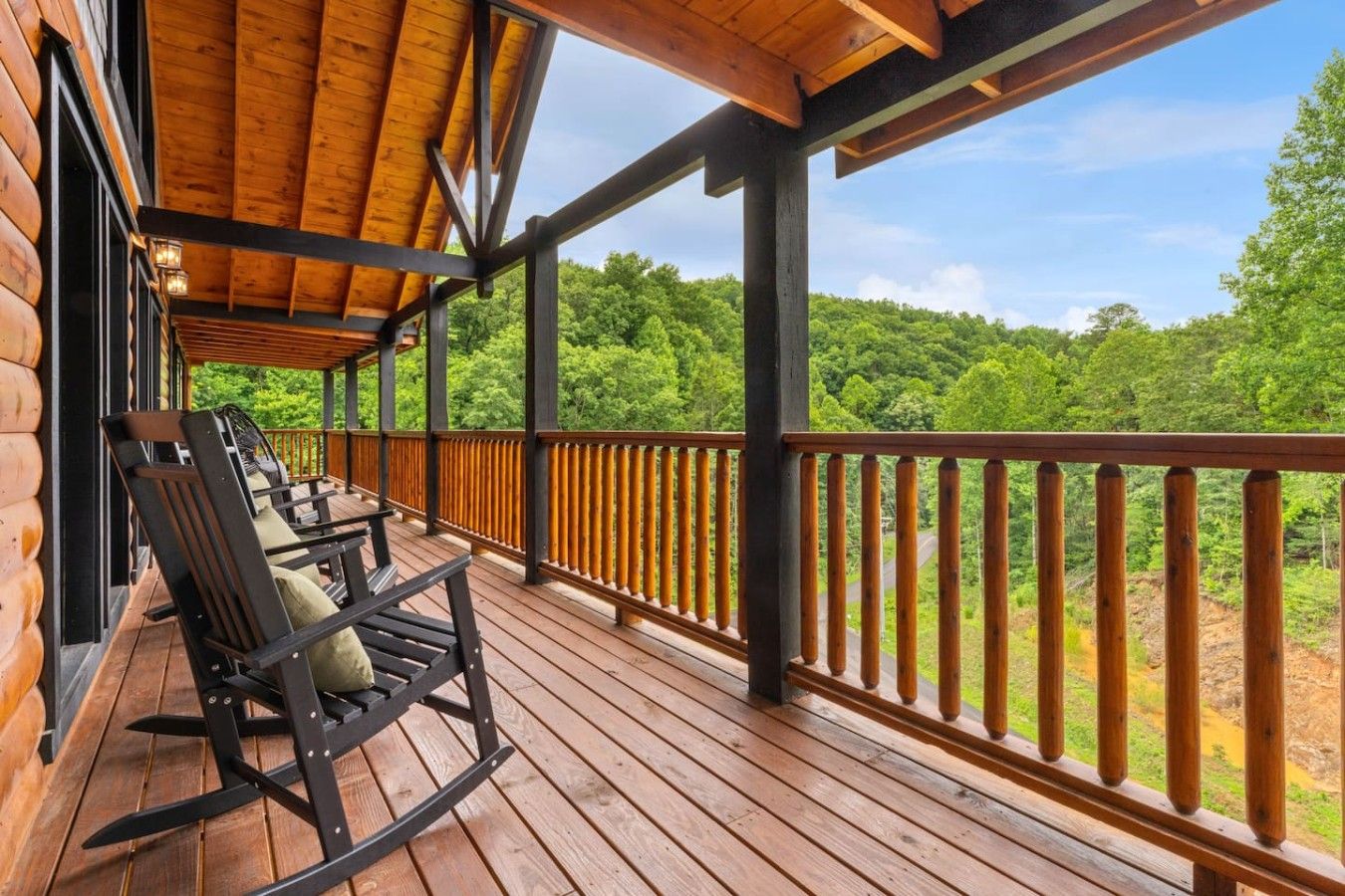 Une terrasse en bois avec une balustrade, un fauteuil à bascule et une vue sur un paysage boisé.