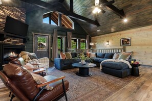 A cozy living room with a fireplace, leather chairs, a dark sofa set, and a stone wall. - Pool, Hot tub, Game Room, Gazebo, Sleeps 36 (Sevierville)
