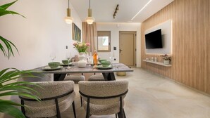 Un espace de salle à manger moderne avec une table dressée pour quatre personnes, des chaises, des luminaires suspendus, un téléviseur à écran plat fixé au mur et un mur recouvert de panneaux en bois.