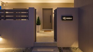 Une entrée moderne avec une allée fermée par un portail, un pot de fleurs et une enseigne indiquant « MS MANOLIS ».