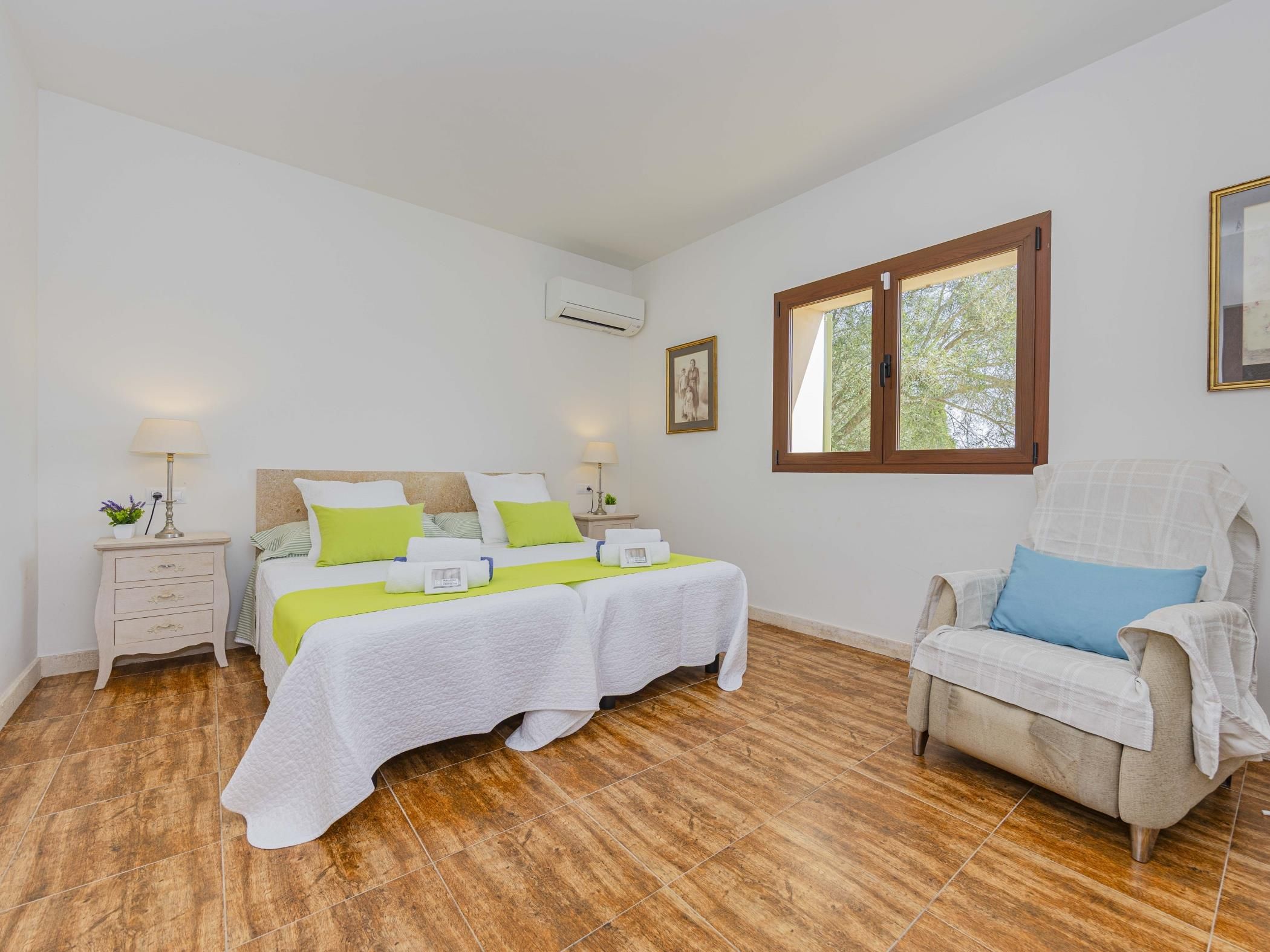 A bedroom with a bed, a chair, a nightstand, and a window.