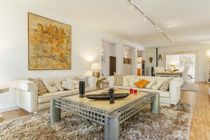 Una sala de estar moderna con un cuadro grande, dos sofás, una mesa de centro y una zona de comedor al fondo.