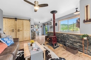 A spacious living room with a large wooden wardrobe, a red wood-burning stove, a cowhide rug, and a view of the outdoors.