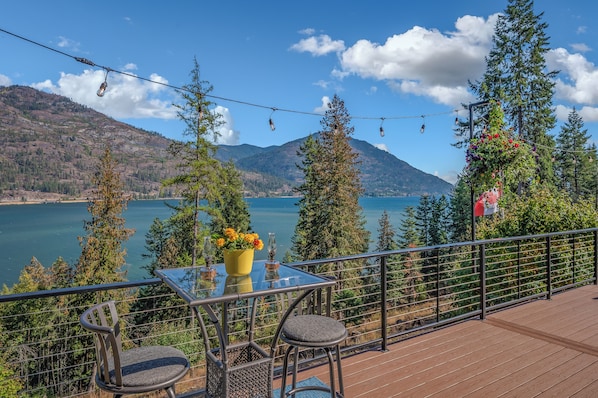 A terrace with a table and chairs, overlooking a lake and mountains.