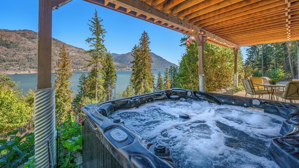 A hot tub under a wooden pergola with a view of a lake and mountains. - SANDBAR LAKE CABIN- Cozy 1-bedroom cabin on 3 very private acres.  (Sandpoint)