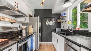 A modern kitchen with a stainless steel refrigerator, a double oven, and a black countertop. - SANDBAR LAKE CABIN- Cozy 1-bedroom cabin on 3 very private acres.  (Sandpoint)