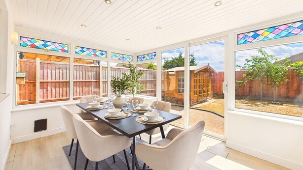 Un coin repas avec une table dressée pour quatre personnes, de grandes fenêtres ornées de vitraux et une vue sur le jardin.