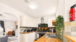 Une cuisine moderne avec des meubles blancs, un plan de travail en bois, une cuisinière et un extincteur.