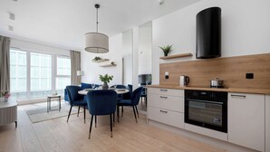 Een moderne keuken met een inbouwoven, een eetgedeelte met blauwe stoelen, en een groot raam met gordijnen.