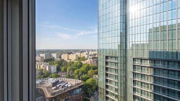 Een hoog gebouw met een moderne glazen gevel, uitzicht op de stad en een glimp van een gebouw met een gebogen dak.