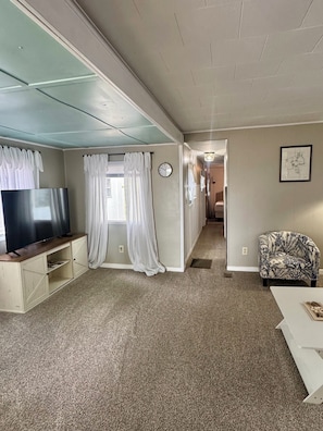 A living room with a TV, a sofa, a patterned armchair, and a hallway leading to another room. - The beach is 30 seconds away! Chapman Lake in Warsaw, IN. (Warsaw)