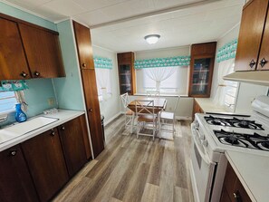 Cocina compacta con armarios de madera, una encimera blanca, una mesa de comedor con sillas y una estufa blanca.