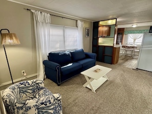 A living room with a blue sofa, a white coffee table, a patterned armchair, a lamp, and a kitchen area with a refrigerator and dining table. - The beach is 30 seconds away! Chapman Lake in Warsaw, IN. (Warsaw)