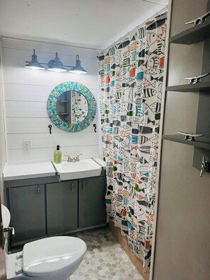 Un baño con un lavamanos blanco, un espejo con marco de mosaico, un inodoro y una cortina de ducha con estampado de peces.