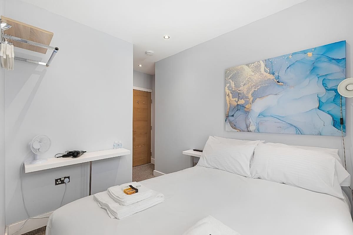 Una habitación de hotel con cama, mesita de noche, una obra de arte en la pared y una puerta de madera.