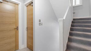 A staircase with a handrail, a wooden door, and a white wall with a light switch. - Blue Door Stay - 5 Bedroom Apartment in London, UK (London)