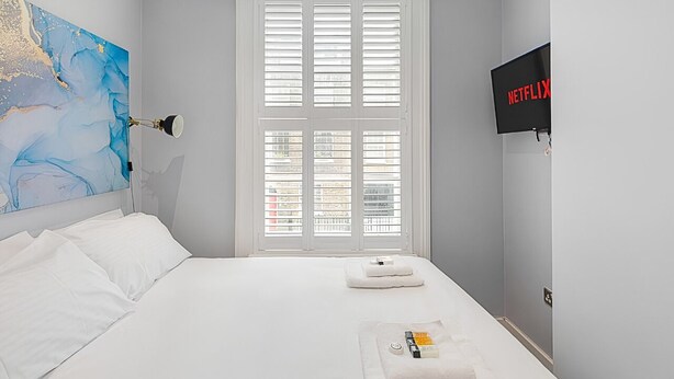 A hotel room with a bed, a map artwork, a TV, and a window with blinds. - Blue Door Stay - 5 Bedroom Apartment in London, UK (London)