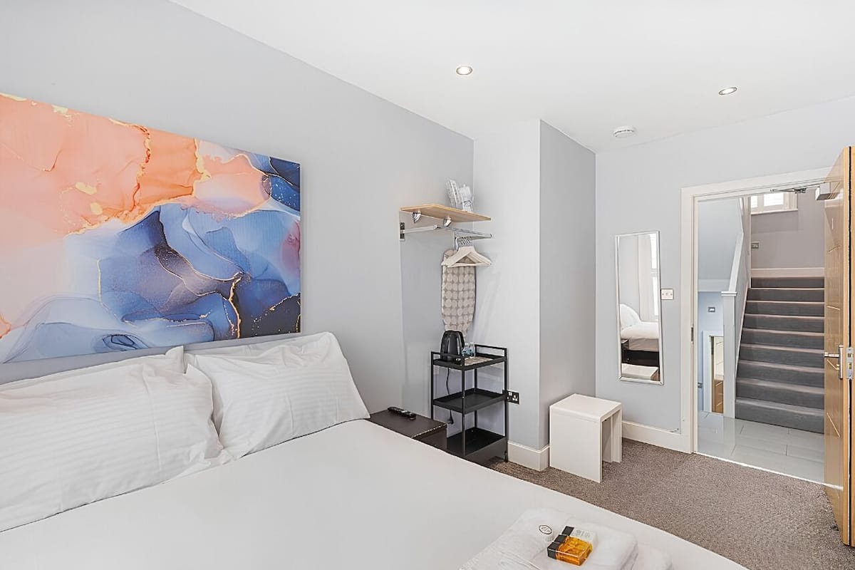 Habitación de hotel moderna con una cama grande, un cuadro en la pared, una mesita con una taza, una mesita de noche y una escalera que lleva a otra habitación.