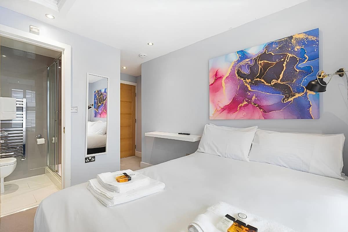 Una habitación de hotel moderna con una cama grande, un baño con ducha de vidrio y un cuadro en la pared.