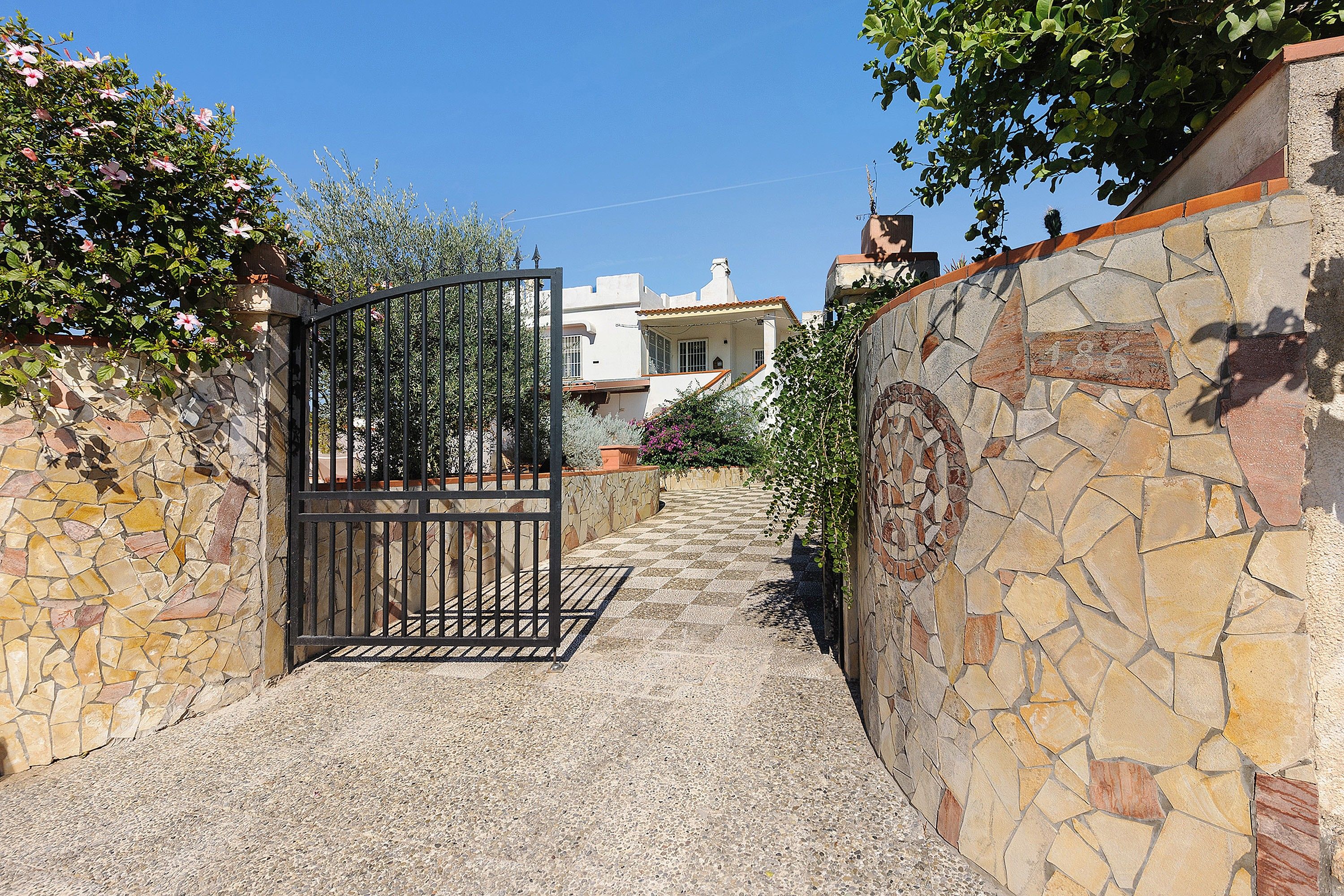 A stone pathway leading to a gated entrance with a building in the background.