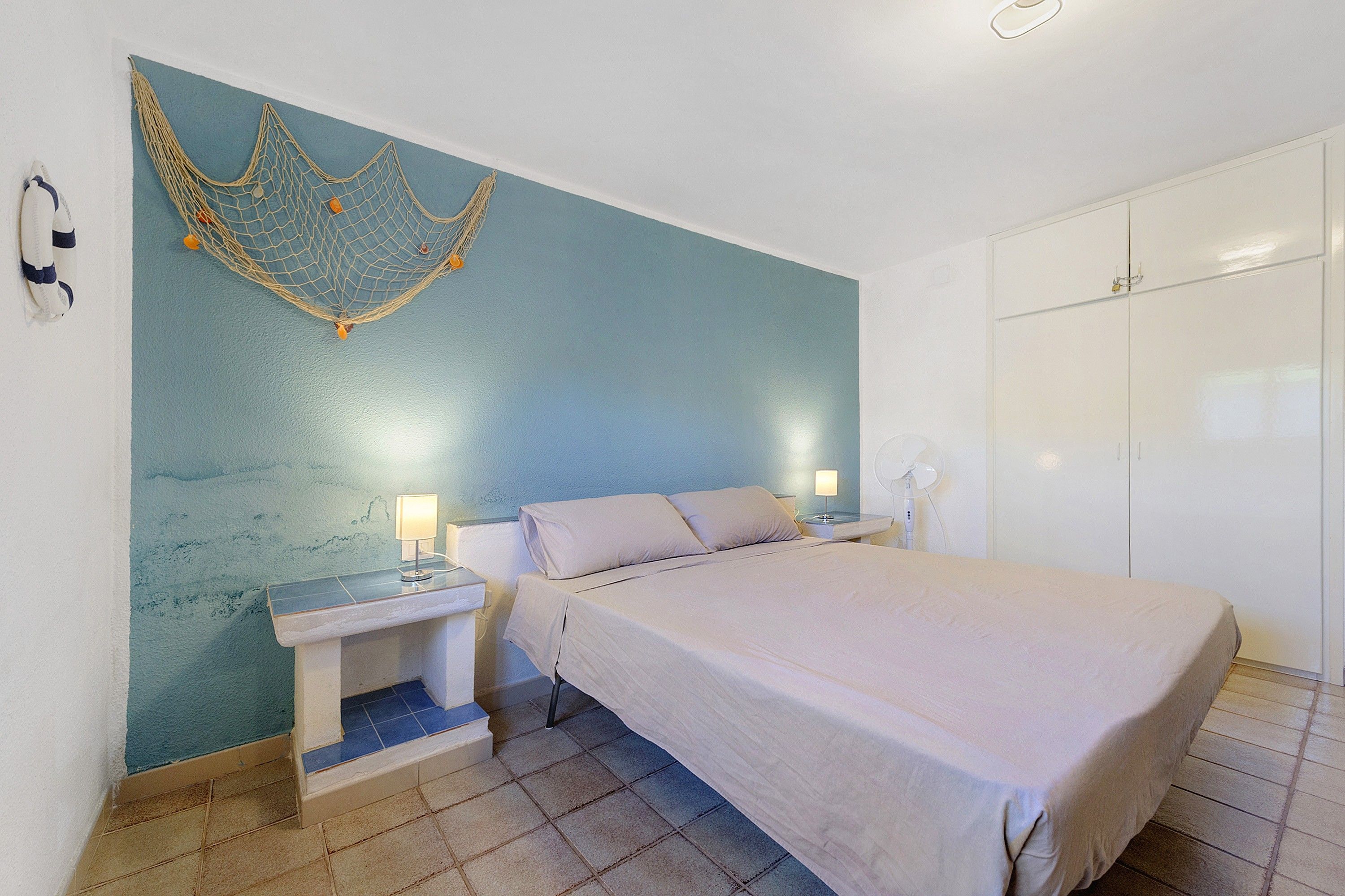 A bedroom with a bed, bedside tables, a wall-mounted light fixture, and a wardrobe.