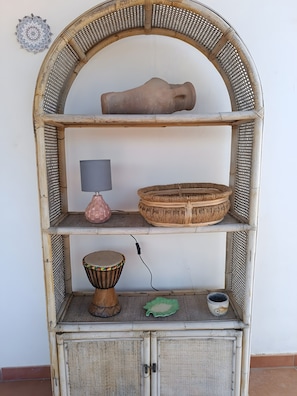 A wicker shelf unit with a pottery piece, a lamp, a woven basket, a drum, and a small decorative item.