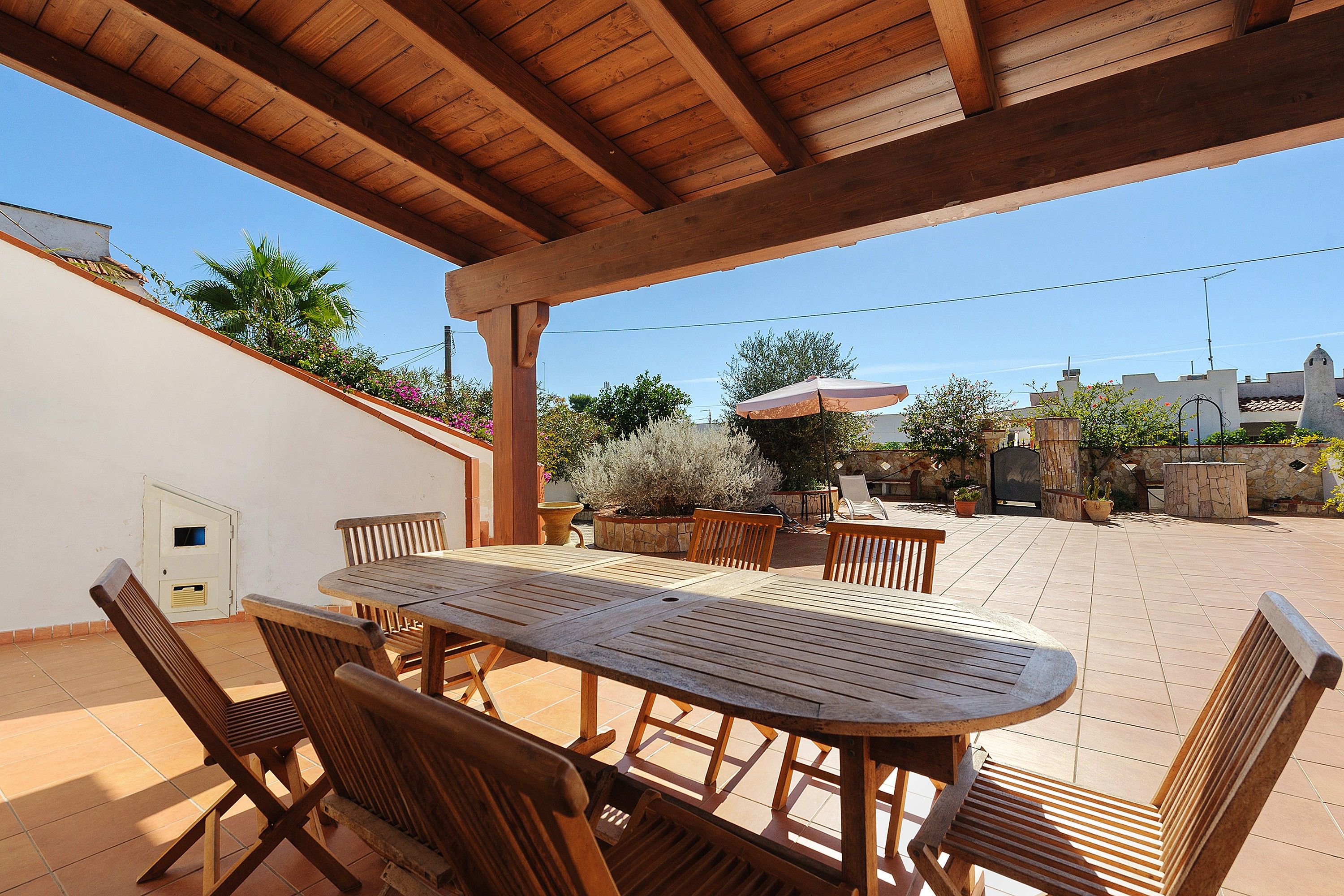 An outdoor patio with a wooden table and chairs, surrounded by potted plants and a stone wall.