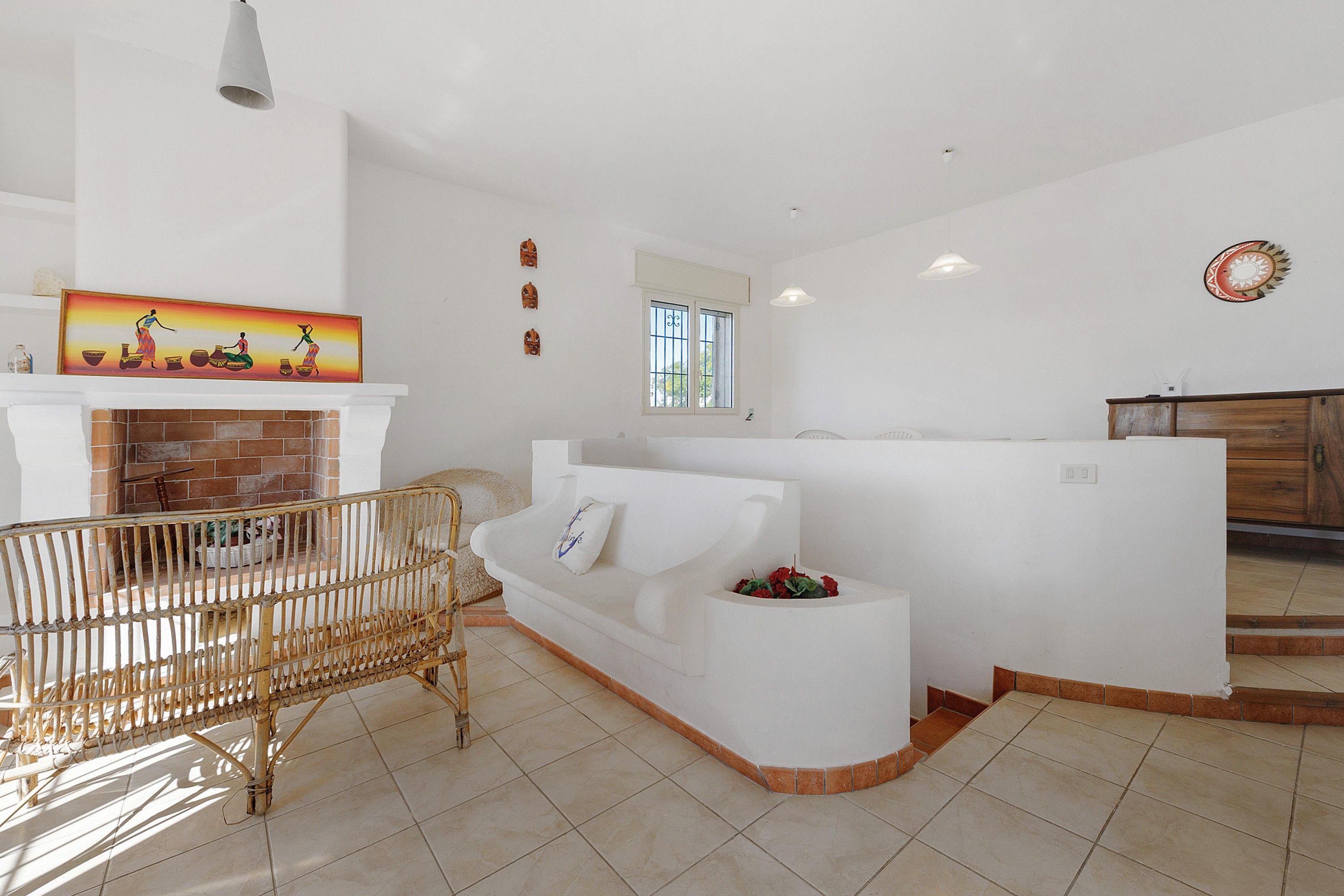 A living room with a white sofa, a wicker chair, a fireplace, and a painting on the wall.