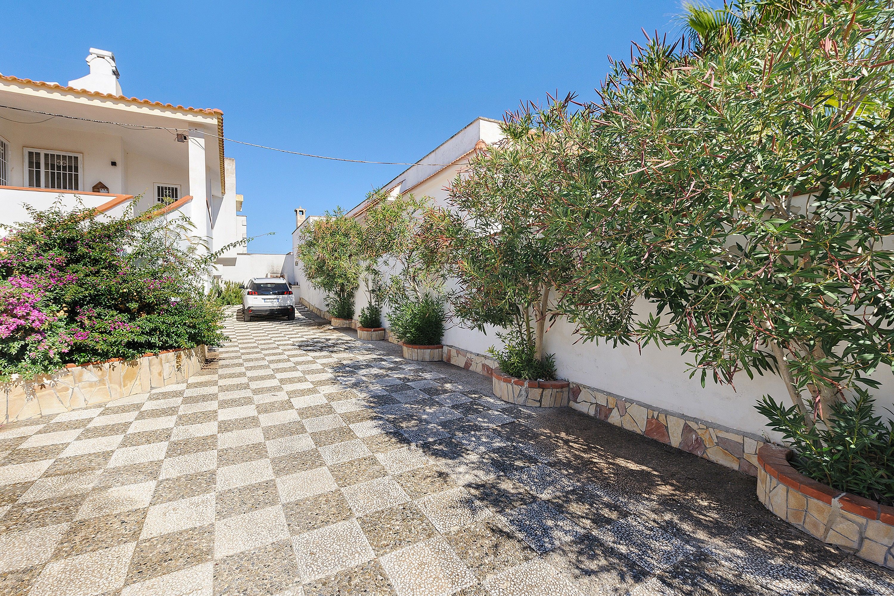 A narrow street with a checkered pavement leading to a white building with a balcony.